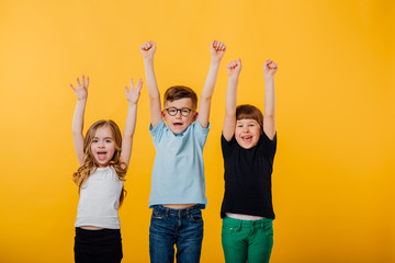 three beautiful children, little boy in glasses and two little girls jumping up, hands raised,...