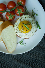 Beef steak with fried egg in spices. Decorated with rosemary, fresh cherry and slices of bread. Filed on a white plate. Dark wooden background. View from above.