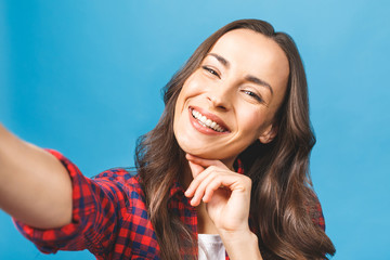 Lovely playful young woman taking selfie with mobile phone isolated over blue background.