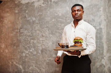 Young african american waiter man hold tray with burger against gray wall.