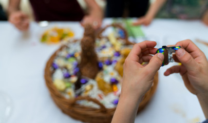 hands of a child unwrap a chocolate candy egg with a large Easter egg basket in the background during Easter cellebrations