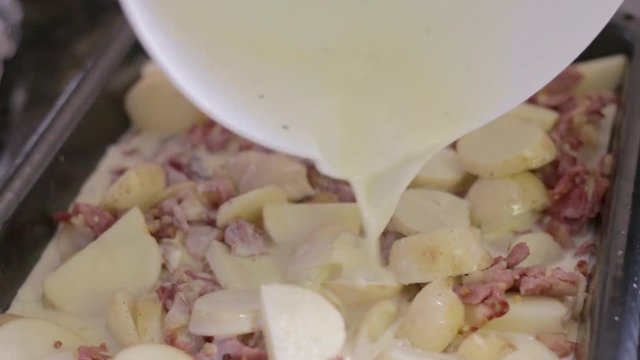 Young woman pouring sauce over potato and bacon dish