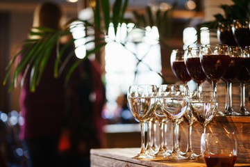 row of transparent wine glasses with drinks on a rack in a bar or restaurant prepared for guests of...