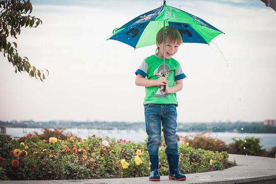 Smiling boy holding an umbrella under rain and sunshine 