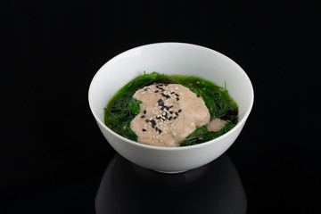 Salad with seaweed and sesame in the dark plate in the center of the black background.
