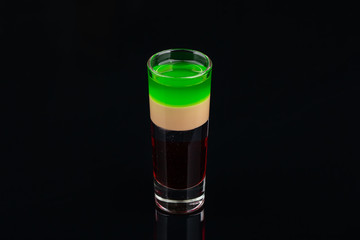 Green alcoholic shot glass with absent, irish cream, liquor on elegant dark black background.