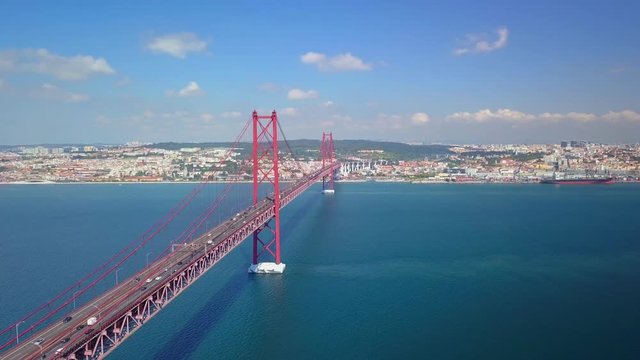 Aerial, drone shot, panning around the Ponte 25 Abril bridge, overlooking road A2, and the downtown of Lisboa city, on a sunny day, on Tejo river, in Lisbon, Portugal