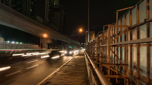 Panning timelapse of Mass Rapid Transit elevated train track and traffic on city road at night.