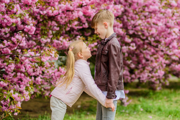 Love is in the air. Couple adorable lovely kids walk sakura garden. Tender love feelings. Little girl and boy. Romantic date in park. Spring time to fall in love. Kids in love pink cherry blossom