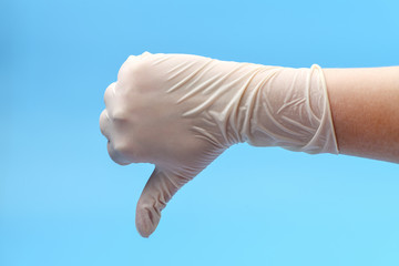 Fragment of a hand in white medical gloves that shows thumb down on a blue background. Show thumb down. Medical background