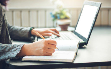 Young asian woman using laptop working and write on note book to make an appointment