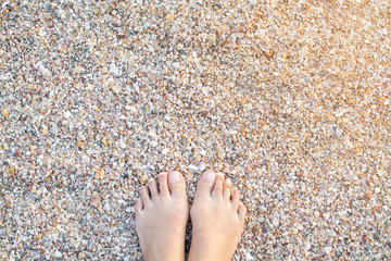 Asian female feet on the beach sand with sea shells, beach of Krabi, Thailand.