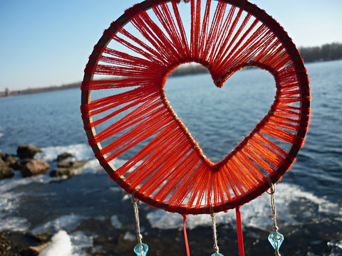Dreamcatcher in the shape of a heart against the background of the river. Dreamcatcher sunset, mountains, boho-chic, ethnic amulet, symbol.