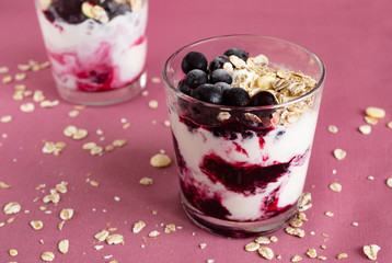 Ice cream with berries and muesli. Ice cream in a glass with currants, berry jam and muesli on a pink background. Close-up.
