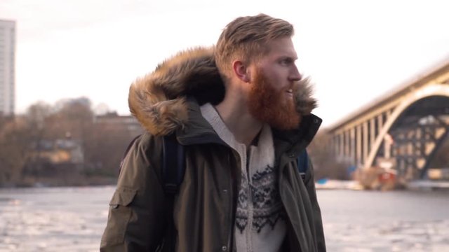 Tall handsome Caucasian male outdoors, cold winter day Stockholm Sweden. Handheld rack pull in slow motion. Beautiful focus pull, attractive bearded hipster man.