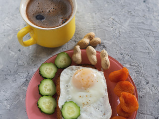 Sandwich with fried egg, nuts, dried apricots and cucumber and a Cup of coffee on a concrete background