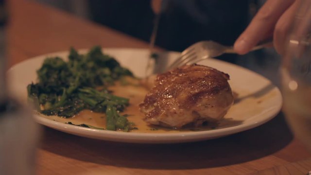 Closeup of a diner slicing a roasted chicken on his plate with his fork and knife