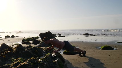 A strong muscular shirtless man doing push up workout at sunrise with ocean waves on the beach of Santa Barbara, California SLOW MOTION.