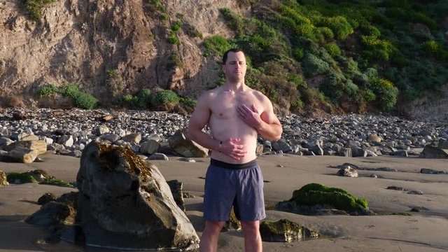 A man doing deep breathing exercises while practicing meditation and mindfulness on the beach at sunrise in Santa Barbara, California SLOW MOTION