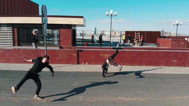 Three athletic young men overcoming obstacles and running on the road performing tricks. Aerial view
