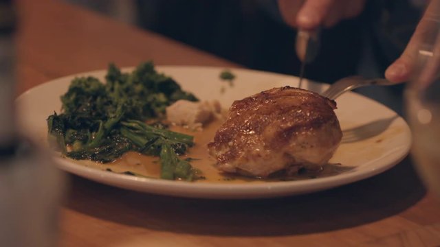 A fork and knife slice off some roast chicken on a plate in a restaurant