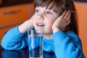 Adorable smiling little girl drinking water in kitchen. Health and beauty concept