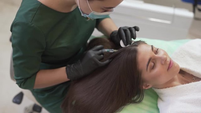Hair Mesotherapy Doctor With Gloves in Hands Injects Natural Plants Extracts and Vitamins on Female Patients Scalp. Light Camera Movement