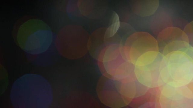 Multicolored spots of shiny bokeh on black background. Stock footage. Colorful bright shiny large bokeh beautifully shine on black background