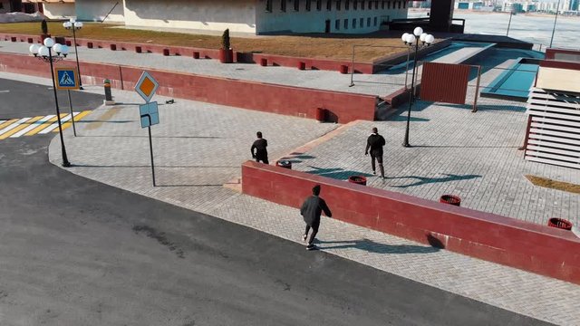 Three athletic young men running on the road and doing tricks. Aerial view