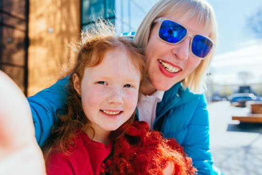 Family couple mature mother in blue eyeglasses and her preschooler red hair daughter together in outdoor activity hugging and enjoying the day before back to school. blonde caucasian mom and girl.