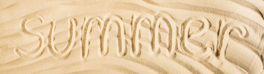 panoramic shot of word summer written on wavy sand