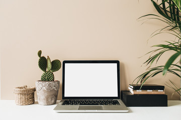 Minimalist home office desk workspace with laptop, cactus, palm on beige background. Front view...