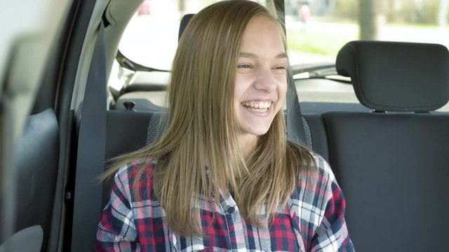 Teen girl sitting in the back seat of car. Happy child enjoying leisure in automobile during sunny day road trip.
