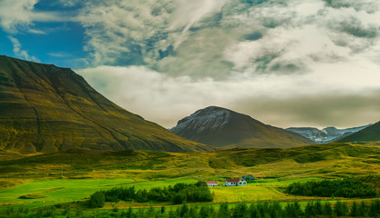 Fototapeta premium Small houses in the valley among the mountains. Typical Icelandic landscape. A beautiful view of secluded housing.