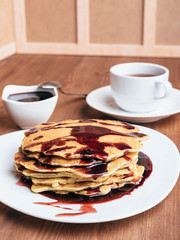 Pancakes with cherry syrup. Tea. Wooden table.