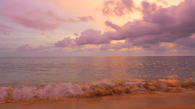 medium wide locked shot of golden twilight hour on a tranquil beach from lower angle showing a calm ocean and romantic clouds and reflections, vanilla orange violet sky, perfect copy space background