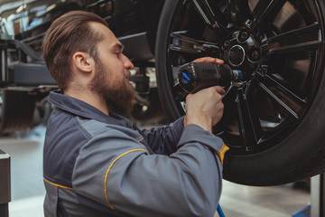Bearded male car mechanic torquing the lug nuts of a wheel of a lifted car at his garage....
