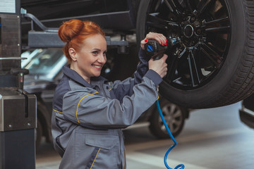 Beautiful cheerful female mechanic smiling joyfully, torquing the lug nuts of a wheel, using...
