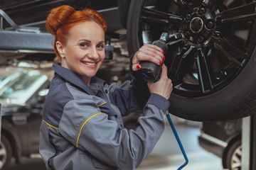 Beautiful red haired female mechanic smiling to the camera over her shoulder, holding electric...