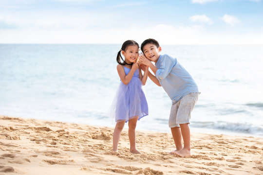 Two children listening to seashell on beach