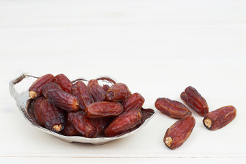 Islamic festival of Ramadan concept. with a delicious tropical dates on a silver plate and shiny rosary on a white wooden table background. Traditional Middle East culture. Ramadan Kareem.