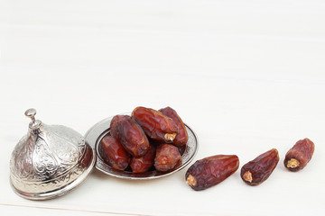 Islamic festival of Ramadan concept. with a delicious tropical dates on a silver plate and shiny rosary on a white wooden table background. Traditional Middle East culture. Ramadan Kareem.