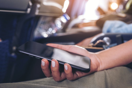 Closeup image of a woman holding a black smart phone while sitting in the cabin