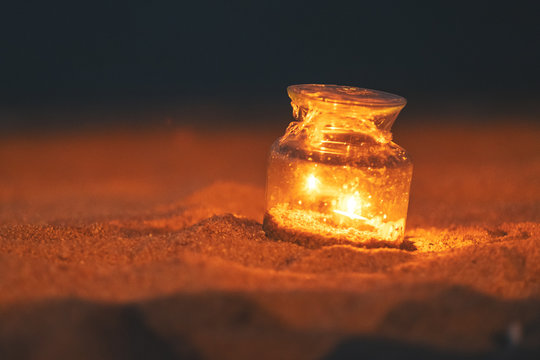 Closeup Image Of A Glass Bottle Candles Holders On The Beach At Night