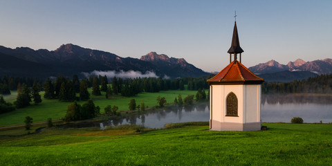 Fototapeta na wymiar small chapel at lake with mountains in the background