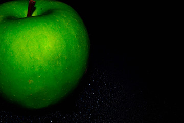 Green ripe apple with water droplets on a dark background, closeup
