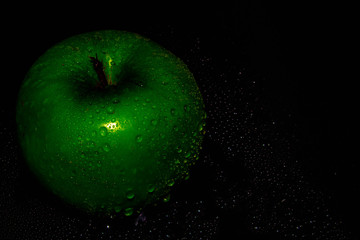 Green ripe apple with water droplets on a dark background, closeup