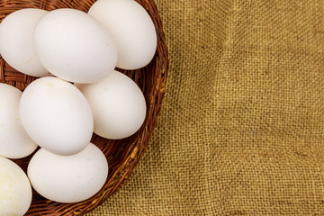 White chicken eggs in wicker basket on sackcloth background