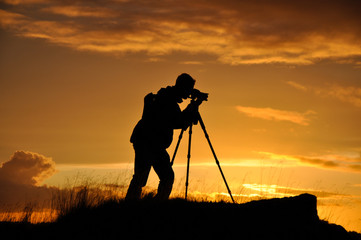 Silhouette of photographer with tripod against setting sun