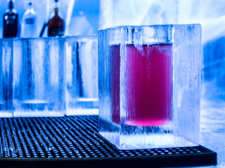 Close up of red drink in glass made of ice in ice bar with other ice glasses in...